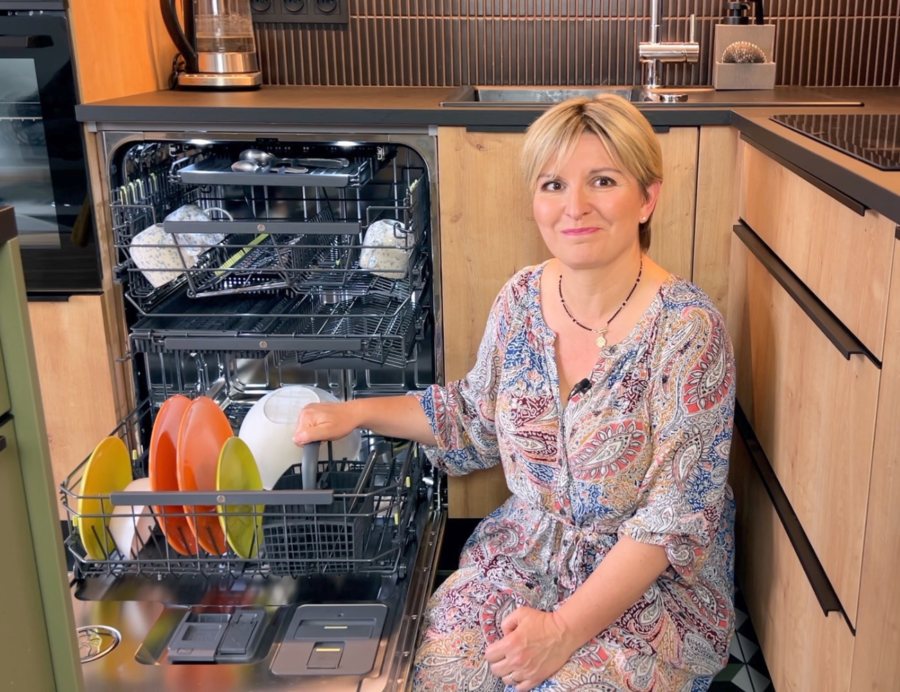 na zdjęciu Pani AGD obok otwartej i wypełnionej naczyniami zmywarki do zabudowy ASKO DFI777UXXL